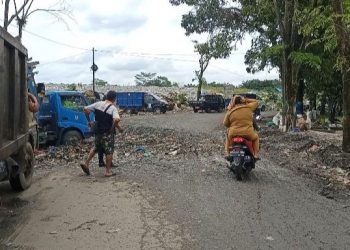 Dua perempuan berseragam ASN tengah melintas dari badan jalan yang berlubang dan dipenuhi rembesan sampah TPA Tanjung Pinggir, Senin (17/5/2021). (isiantar/nda).