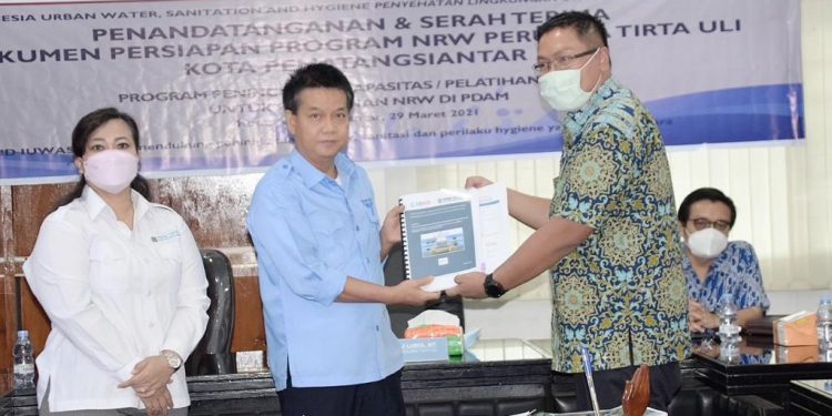 Direktur Utama Perumda Tirtauli Ir Zulkifli Lubis MT didampingi Direktur Umum Perumda Tirtauli Berliana Napitu menyerahkan Dokumen Persiapan Program Non Revenue Water (NRW) dengan IUWASH PLUS.