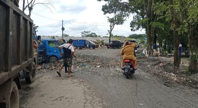Dua perempuan berseragam ASN tengah melintas dari badan jalan yang berlubang dan dipenuhi rembesan sampah TPA Tanjung Pinggir, Senin (17/5/2021). (isiantar/nda).